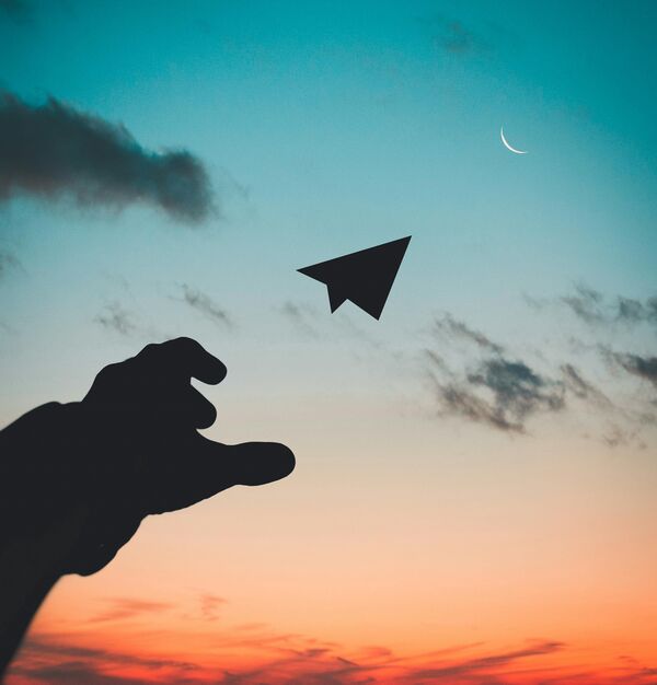 main projetant un avion en papier dans le soleil levant : symbole du futur